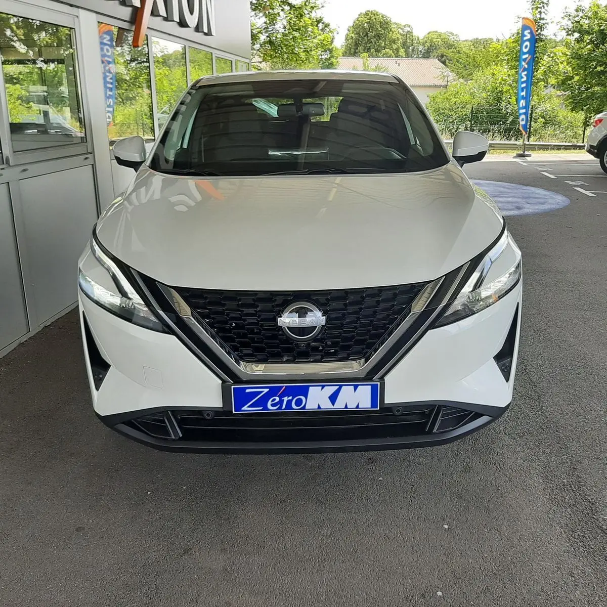 Vue frontale d'un Nissan Qashqai blanc lunaire 2022 avec calandre noire et plaque Zéro KM visible.
