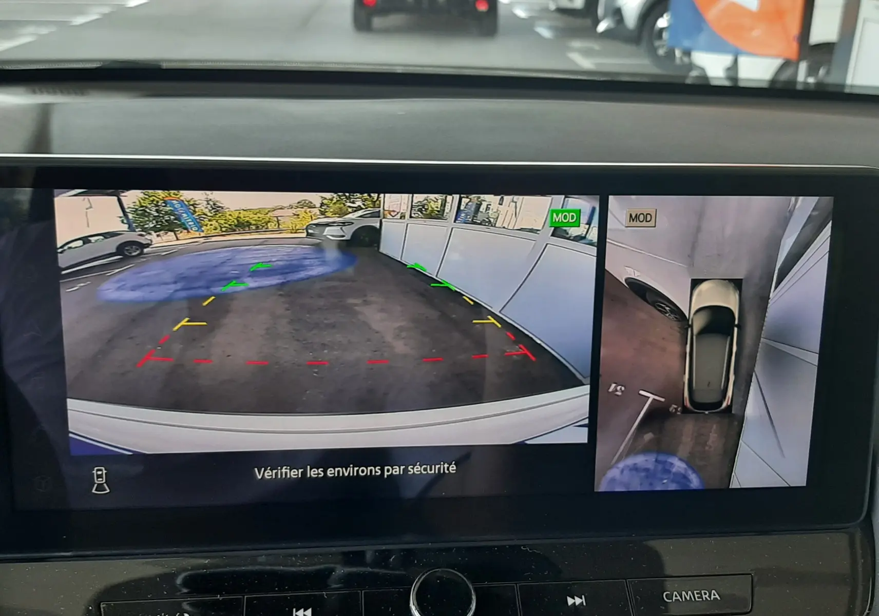 Écran de caméra 360° du Nissan Qashqai blanc lunaire montrant une vue arrière et une vue plongeante du stationnement.