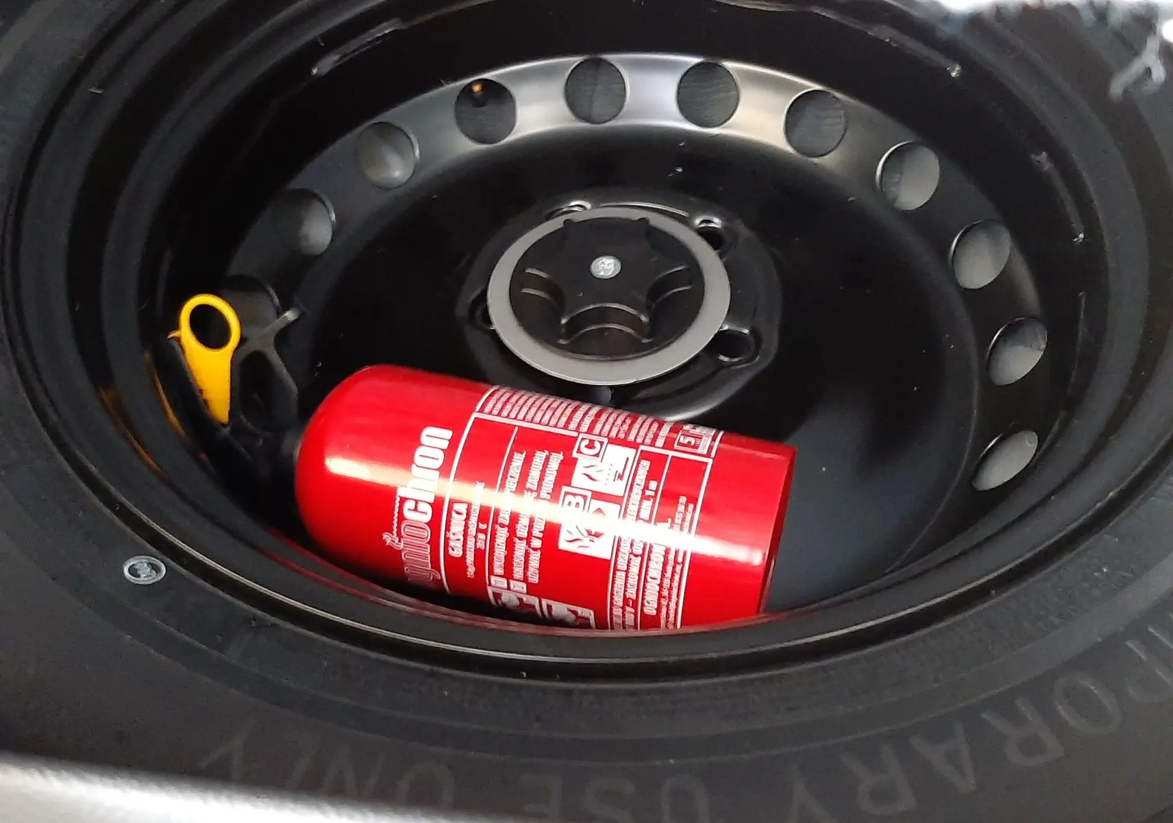 Extérieur du pneu de secours noir du Nissan Qashqai blanc lunaire avec un extincteur rouge posé à l'intérieur.