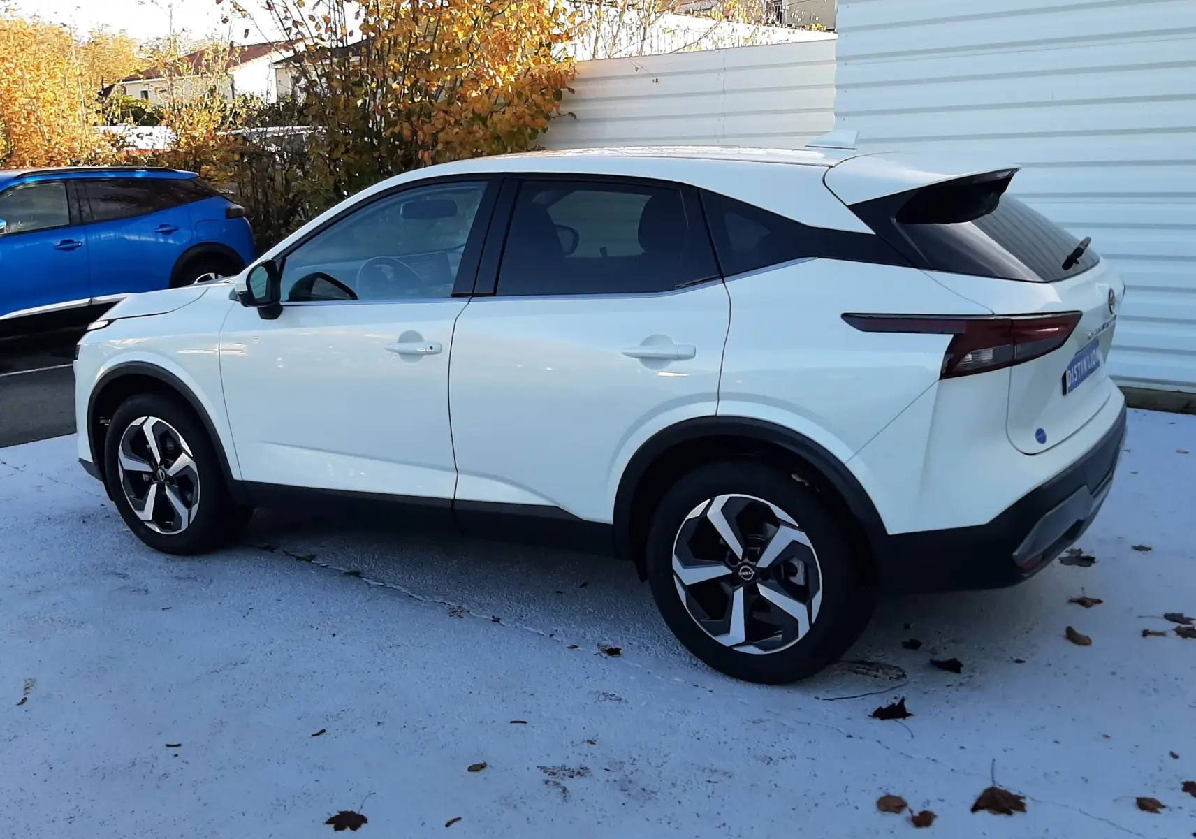 Vue côté gauche arrière d'un Nissan Qashqai blanc lunaire 2022 avec jantes noires et toit noir contrasté.