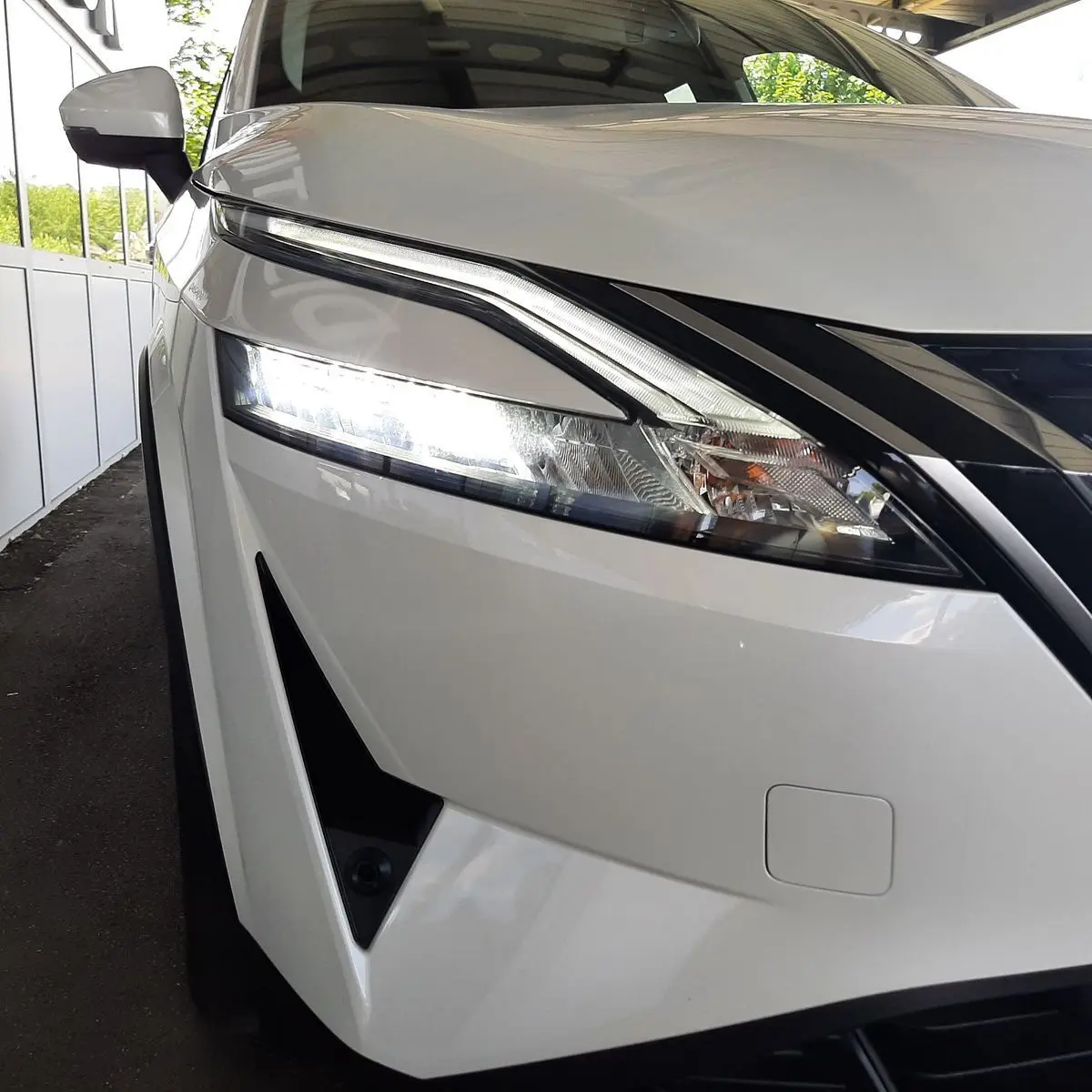 Gros plan sur le phare avant gauche allumé du Nissan Qashqai blanc lunaire 2022, soulignant son design moderne.
