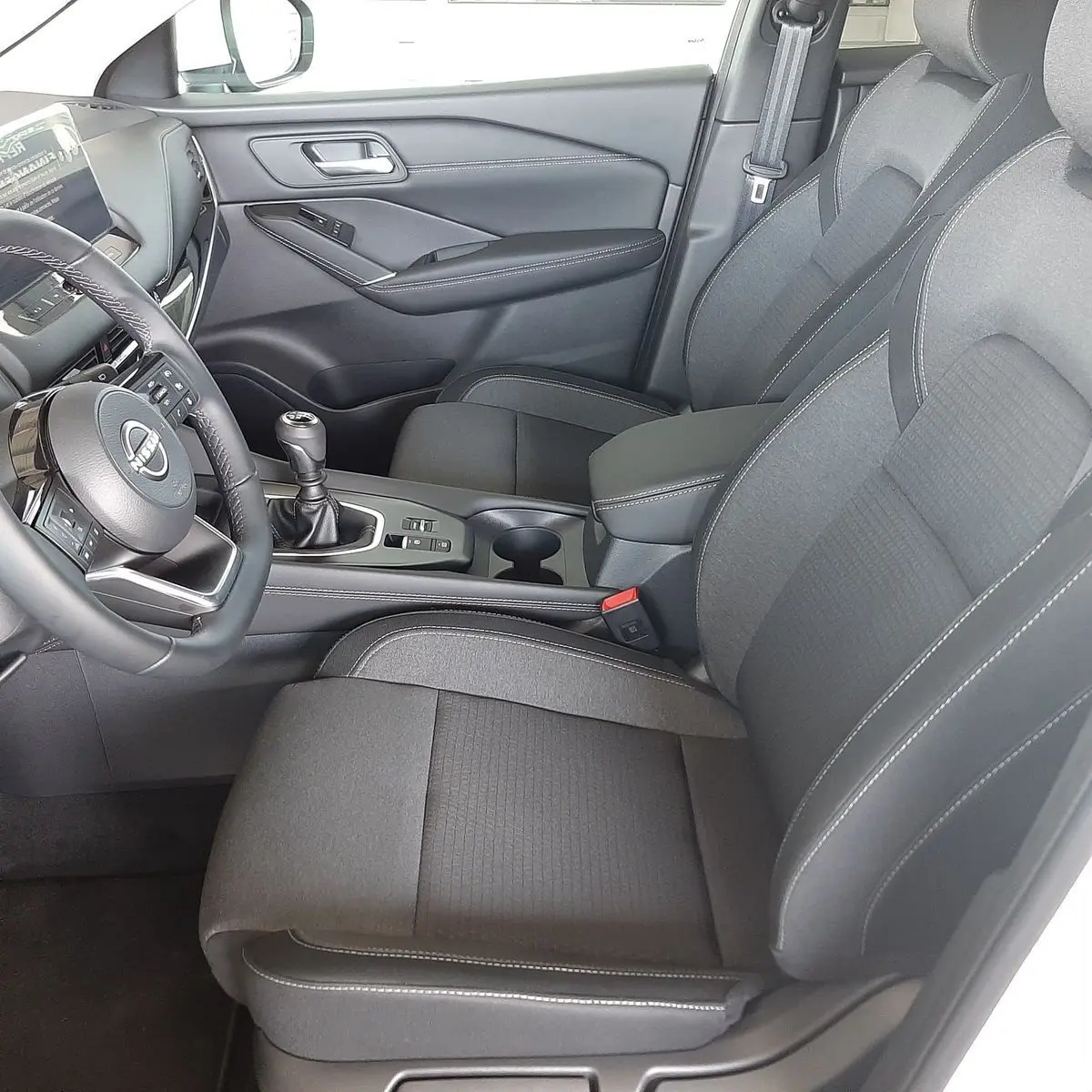 Vue intérieure côté conducteur du Nissan Qashqai 2022 avec sièges en tissu gris et levier de vitesses manuel.