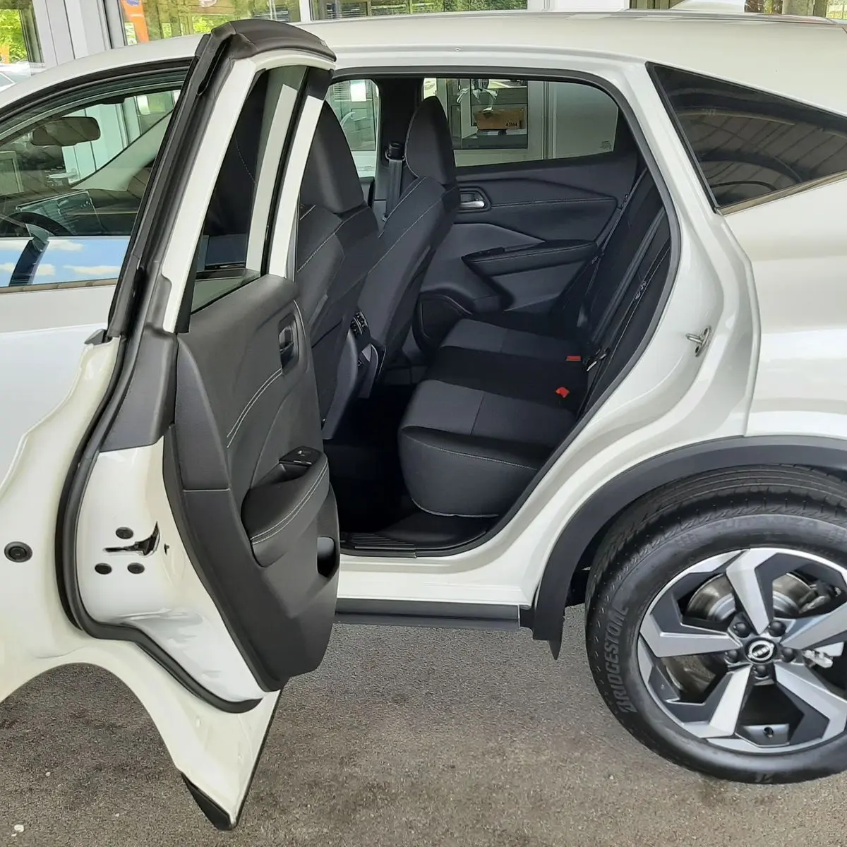 Vue côté gauche arrière du Nissan Qashqai blanc lunaire 2022, porte ouverte sur l'habitacle et sièges noirs.