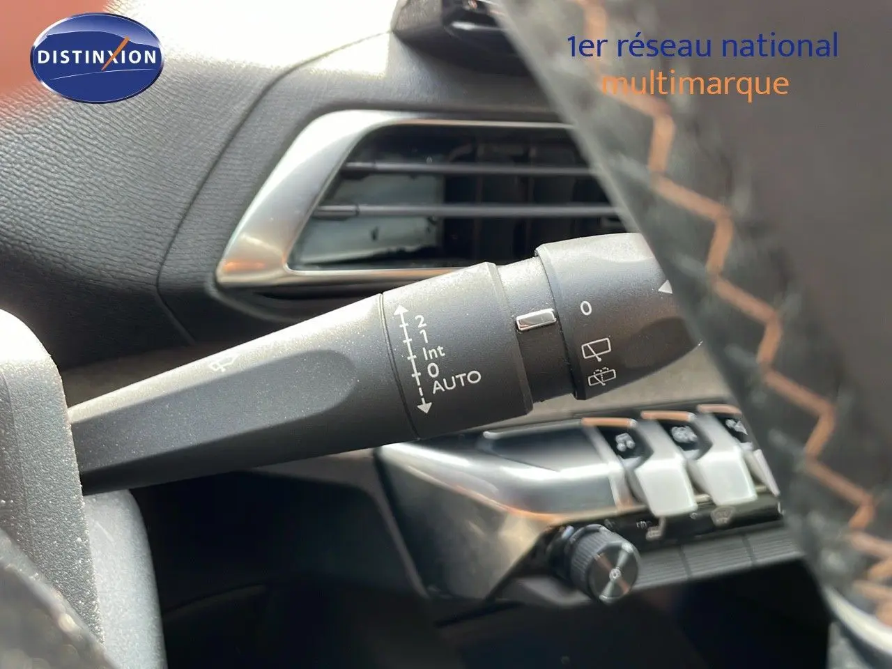 Gros plan sur la commande d'essuie-glace à gauche du volant en cuir noir avec surpiqûres orange du Peugeot 3008 gris platinium.