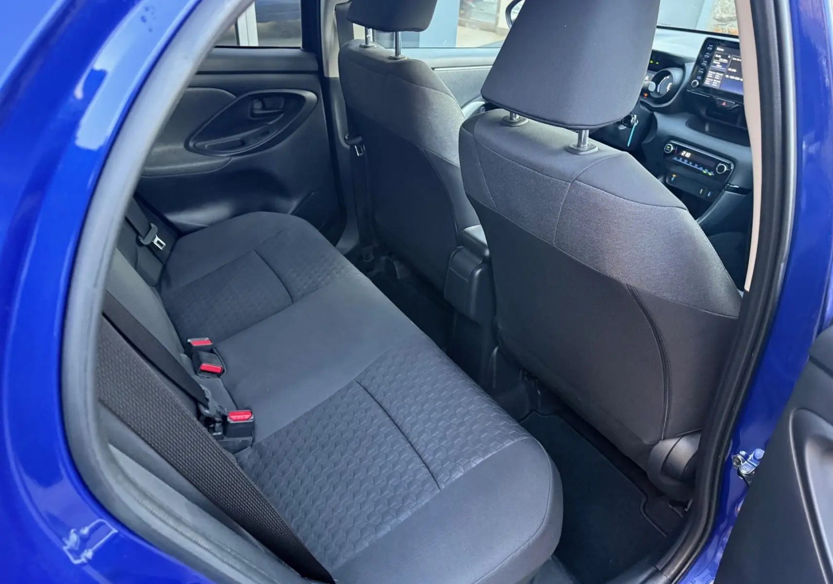 Vue intérieure arrière côté gauche d'une Toyota Yaris Hybride bleu métal 2021 avec sièges tissu gris foncé et console avant visible.