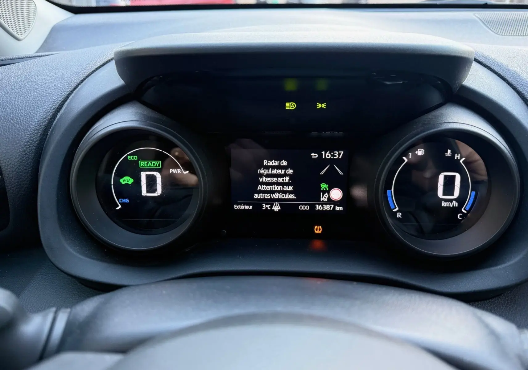 Tableau de bord de Toyota Yaris Hybride bleu métal 2021, affichage numérique du compteur et régulateur actif à 16h37.