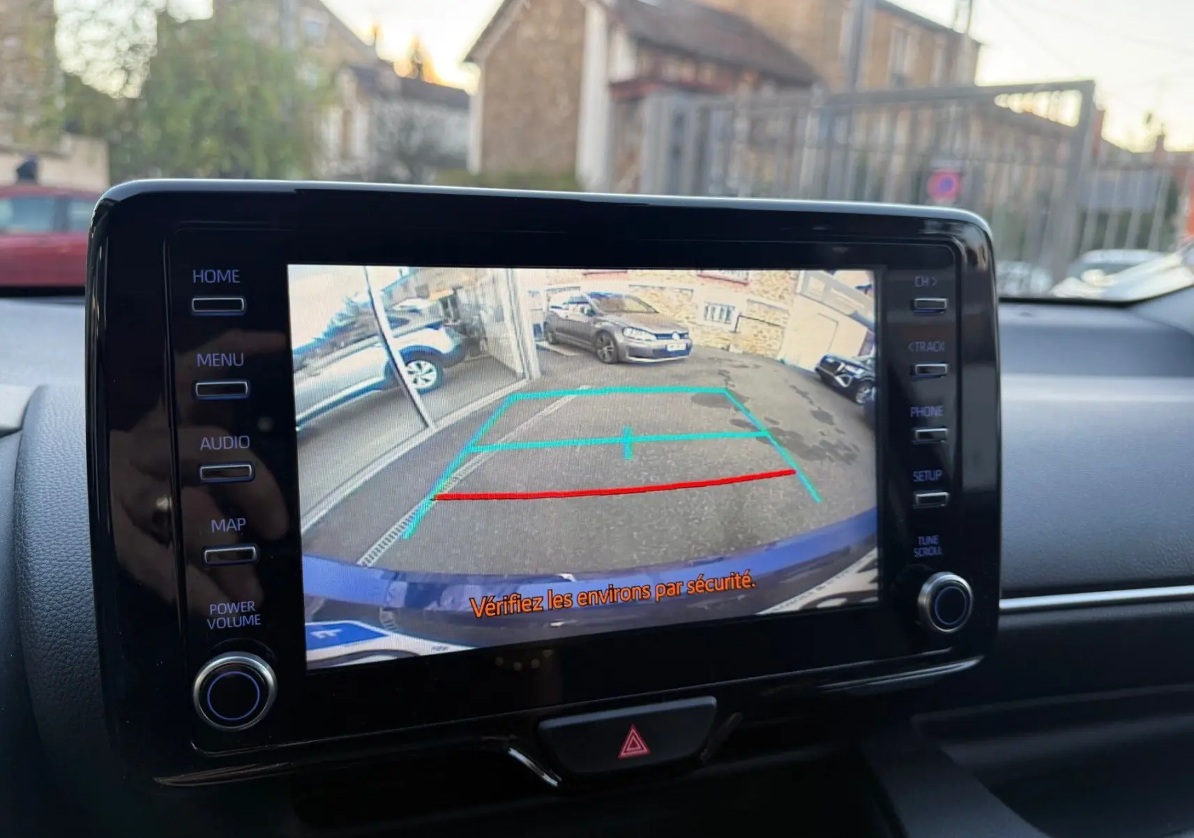 Écran tactile intérieur montrant la caméra de recul d'une Toyota Yaris Hybride bleu métal avec lignes de guidage colorées.
