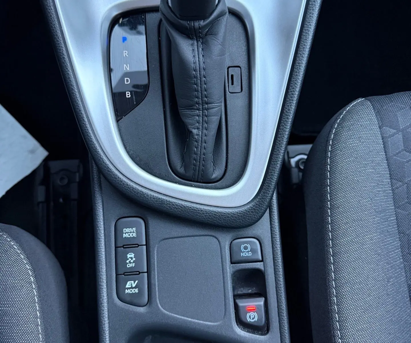 Vue plongeante sur la console centrale de la Toyota Yaris Hybride 2021, avec levier de vitesse automatique et boutons de modes de conduite.