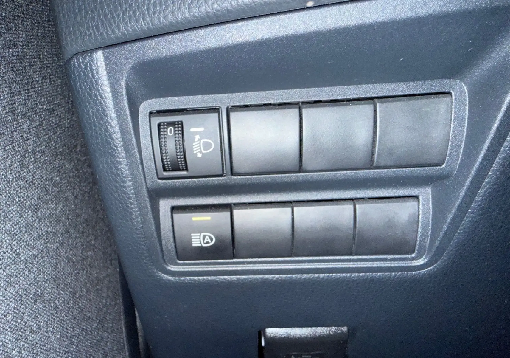 Gros plan sur les commandes d'éclairage et d'assistance situées à gauche du tableau de bord de la Toyota Yaris Hybride bleu métal 2021.