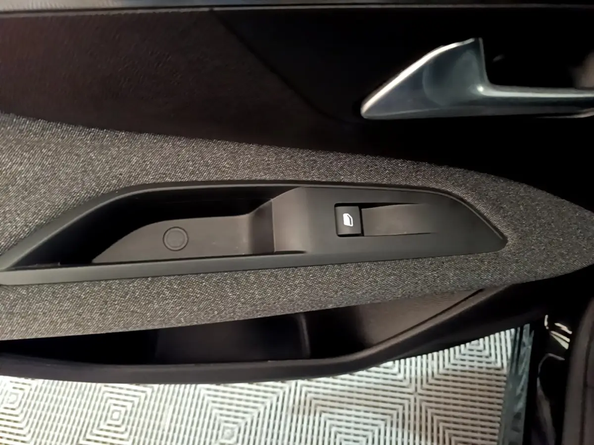 Détail de la commande de lève-vitre côté gauche intérieur d’une Peugeot 3008 noir, tissu gris.