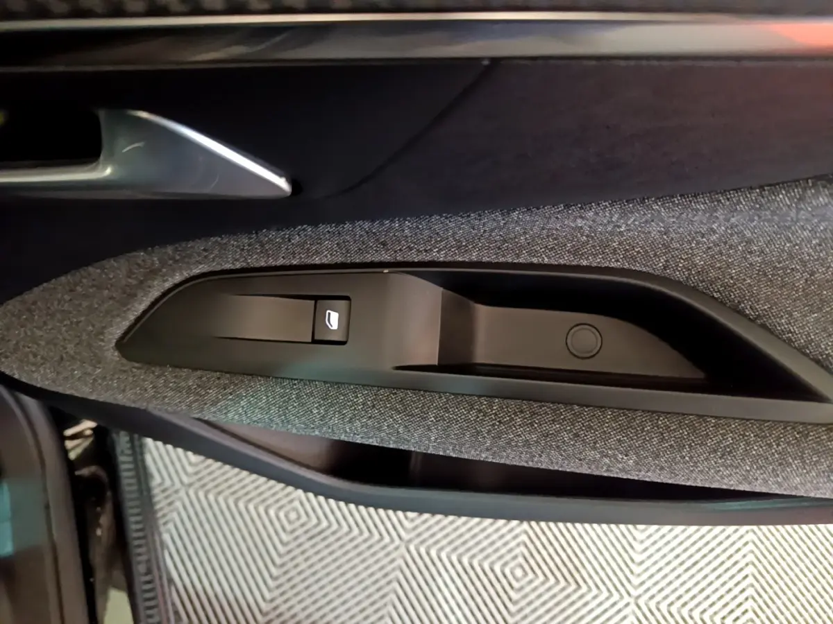Gros plan sur la commande de lève-vitre côté conducteur de la porte intérieure d’une Peugeot 3008 noire, finition tissu gris.