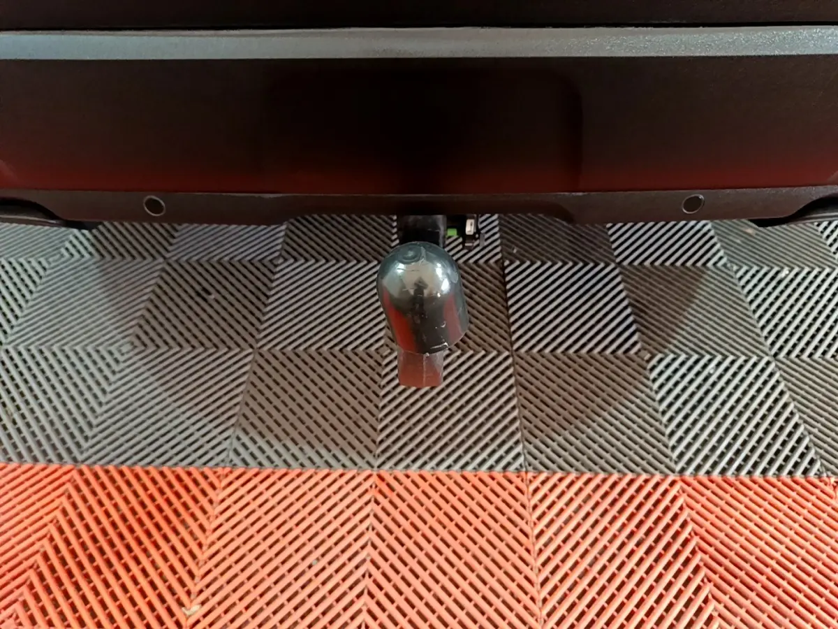 Gros plan sur l'attelage noir du Peugeot 3008 BlueHDi 130 S&S Active Pack, vu de l'arrière sur un sol à damiers gris et rouge.