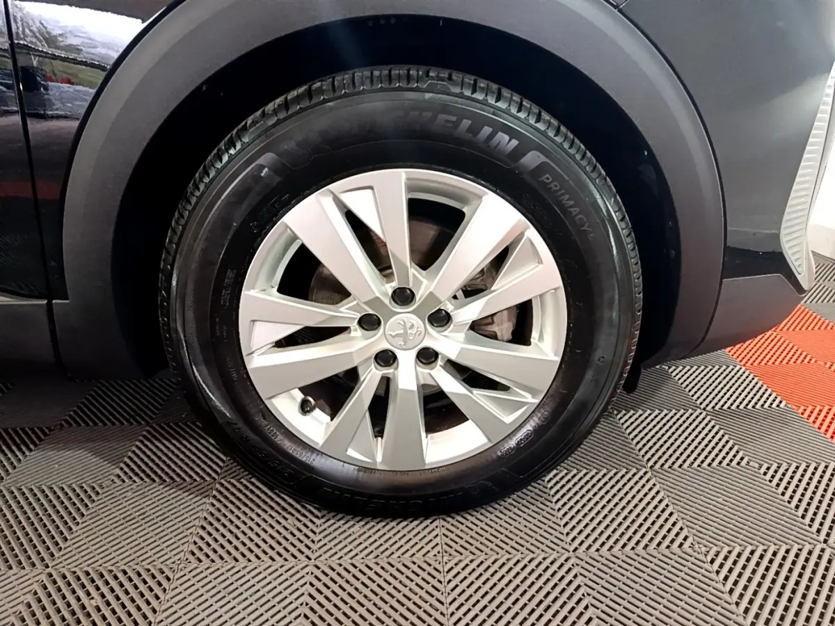 Gros plan sur la roue avant droite d’un Peugeot 3008 noir, mettant en valeur la jante alliage et le pneu Michelin.