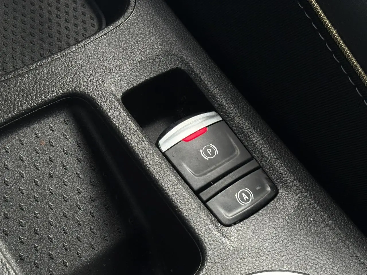 Gros plan sur les commandes du frein de parking électrique et de l’arrêt automatique dans la console centrale noire du Renault Symbioz bleu Iron.