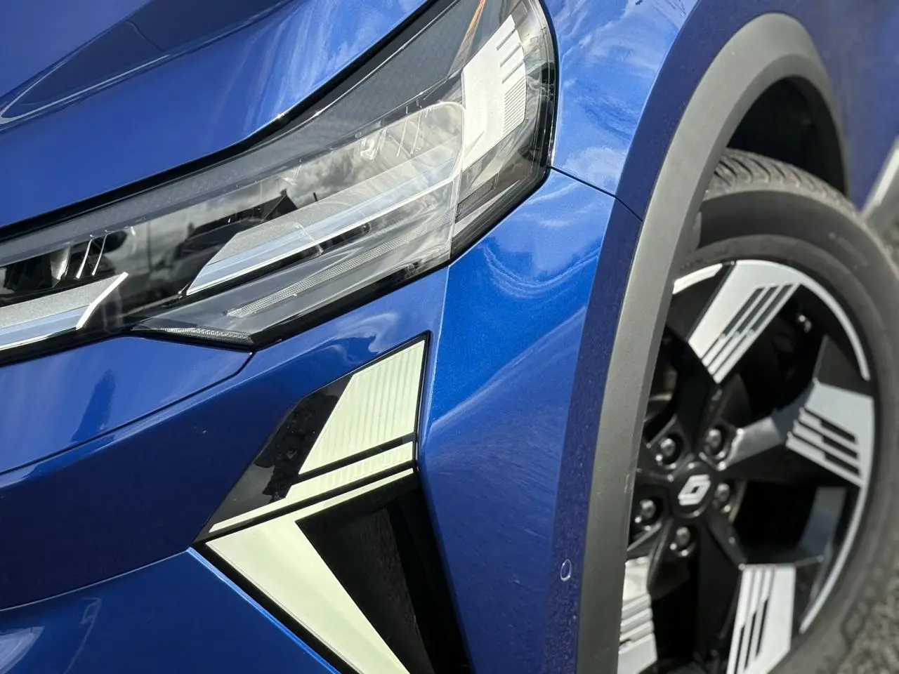 Gros plan sur l’avant droit bleu Iron du Renault SYMBIOZ 2025, mettant en valeur le phare LED et la jante 18 pouces.