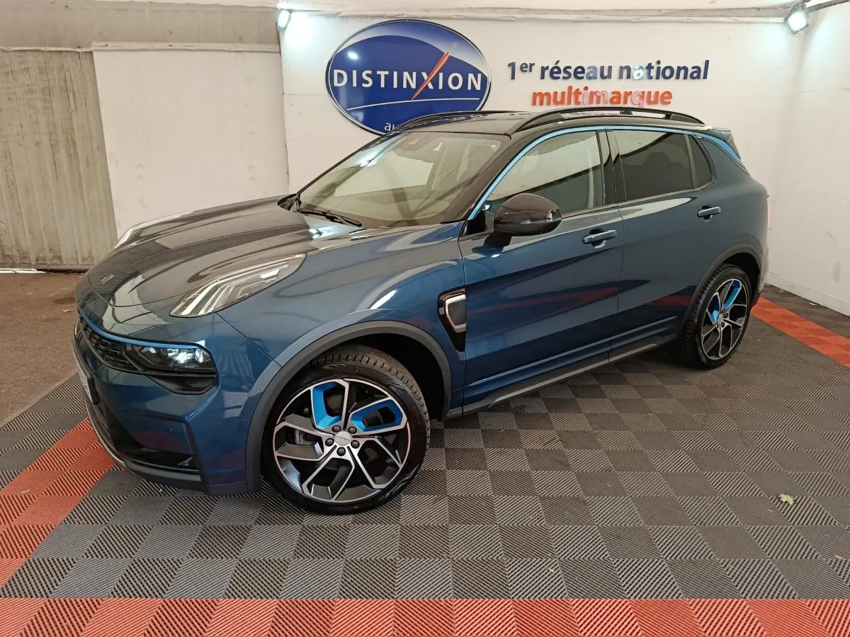 Vue 3/4 avant droite d'un SUV LINK & CO 01 hybride rechargeable bleu avec jantes sport bicolores en intérieur showroom.