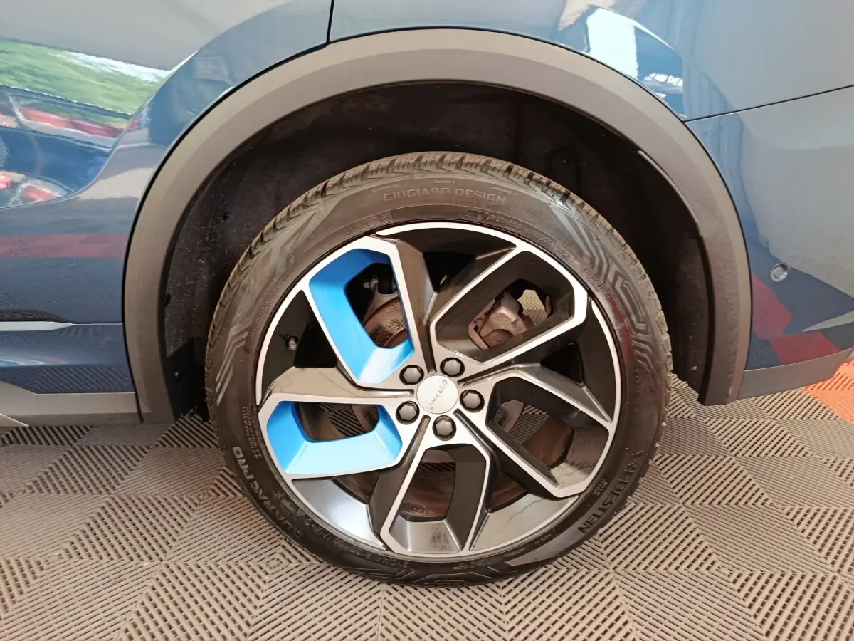 Gros plan sur la roue arrière droite d’un Link & Co 01 bleu avec jante bicolore noire et bleue design Giugiaro.