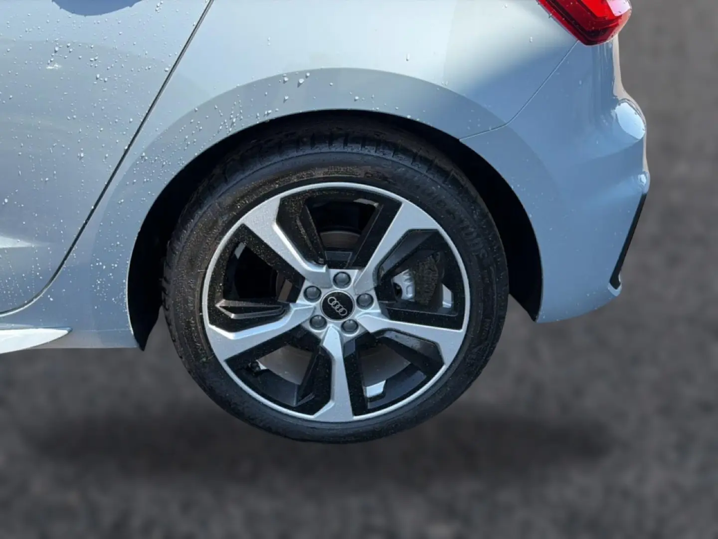 Gros plan sur la roue arrière droite d’une Audi A1 Sportback gris arrow avec jante alu bicolore et carrosserie mouillée.