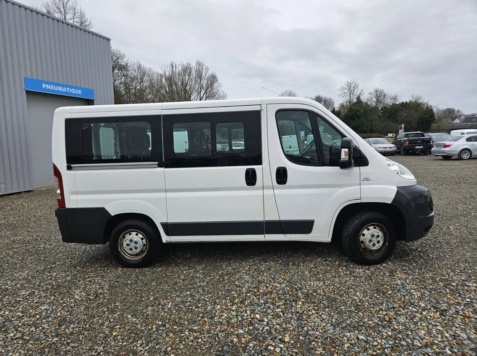 Profil côté gauche d'un FIAT Ducato Combi blanc 2014, fourgon 9 places avec fenêtres teintées et protections noires.
