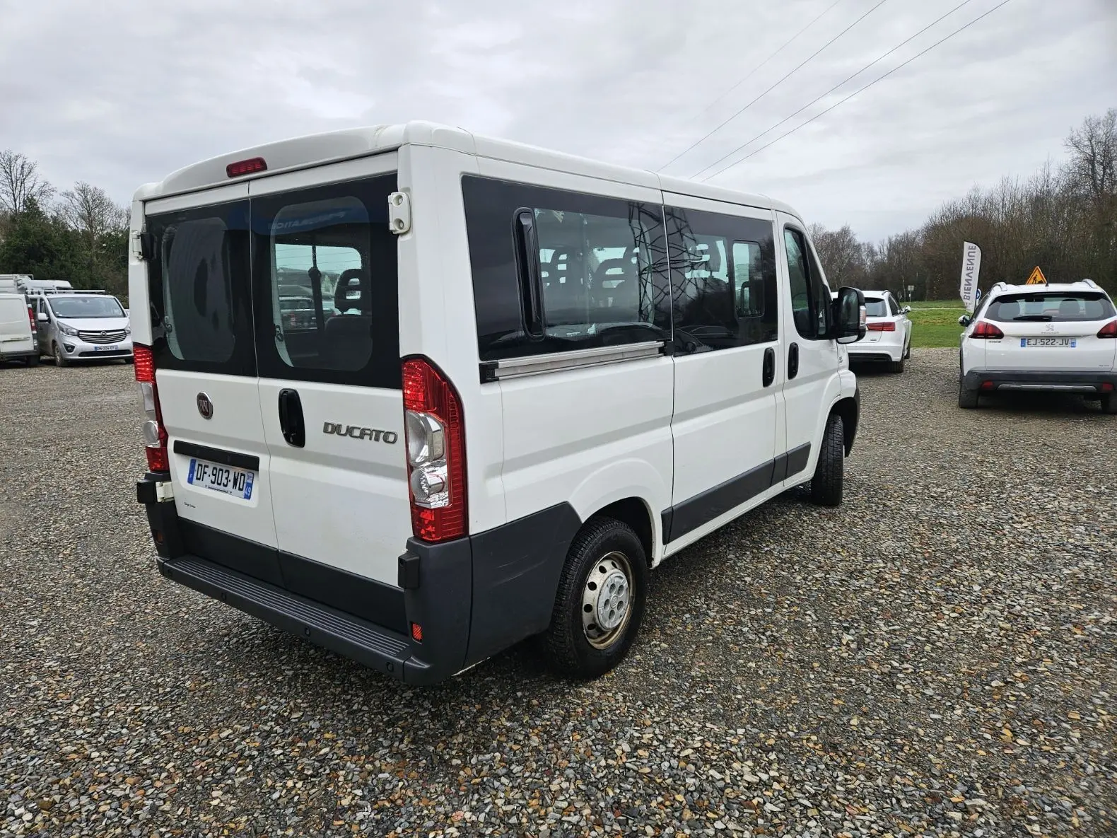 Fiat Ducato Combi blanc vu en 3/4 arrière droit, fourgon 9 places avec vitres latérales teintées et porte arrière double.