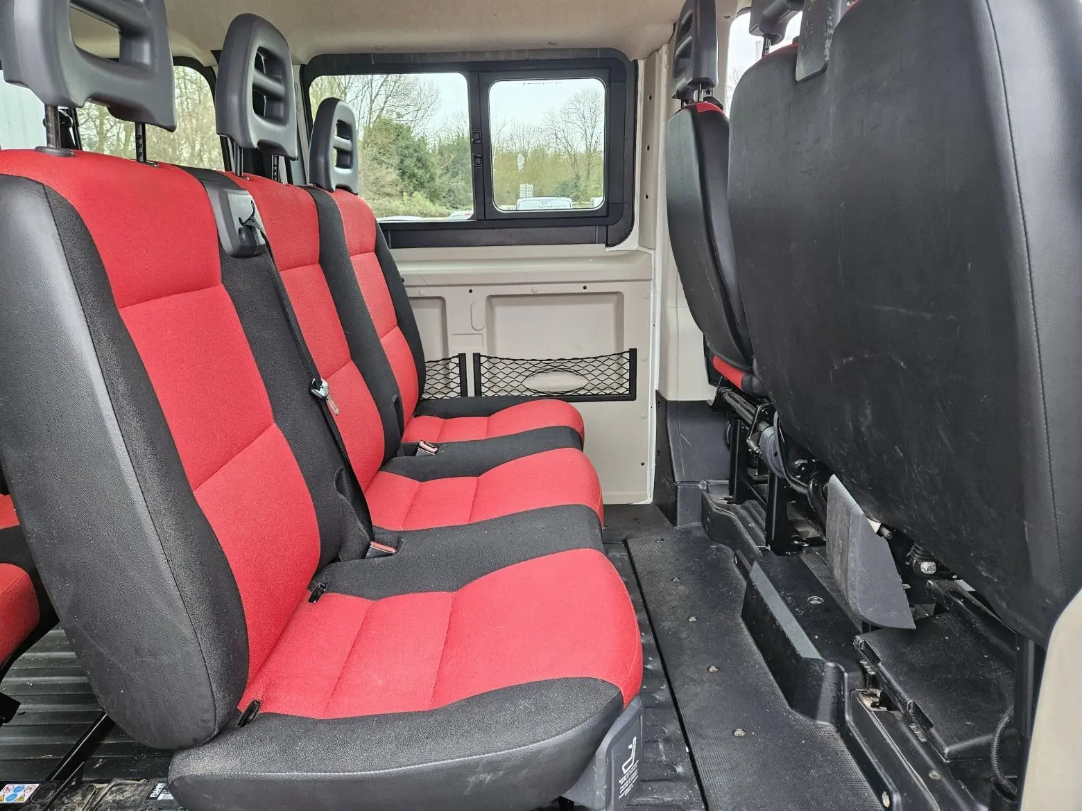Vue intérieure latérale gauche du Fiat Ducato Combi 2014 blanc, sièges rouges et noirs pour 9 places.