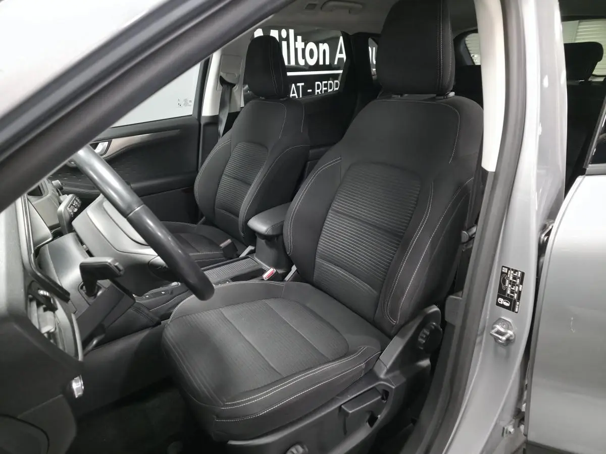 Vue intérieure côté conducteur du Ford Kuga gris 2021, sièges tissu noirs avec coutures blanches visibles.