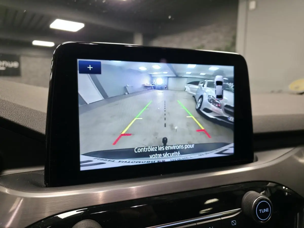 Écran central affichant la caméra de recul du Ford Kuga gris, avec guidage de trajectoire coloré et vue arrière intérieure.