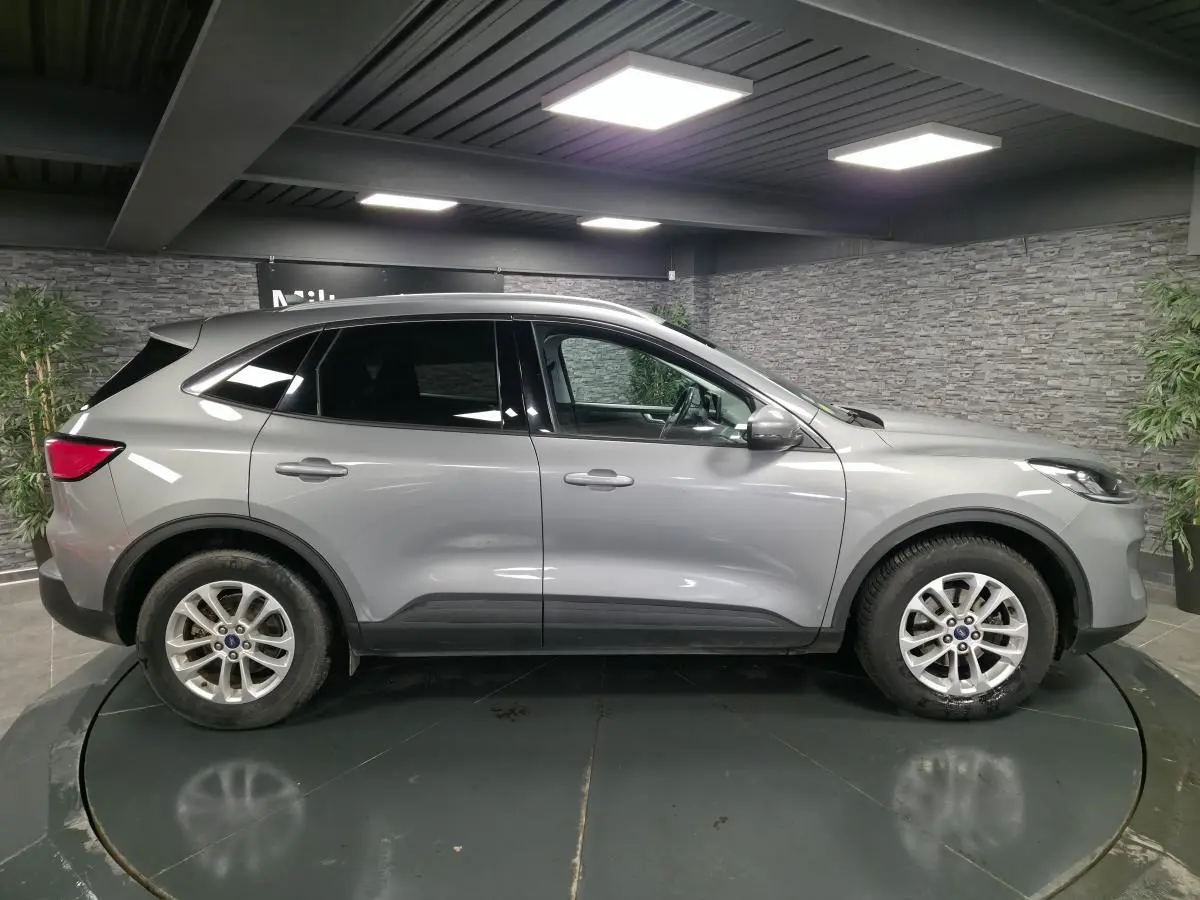 Profil côté gauche d'un Ford Kuga gris métallisé 2021 avec vitres arrière surteintées dans un showroom.