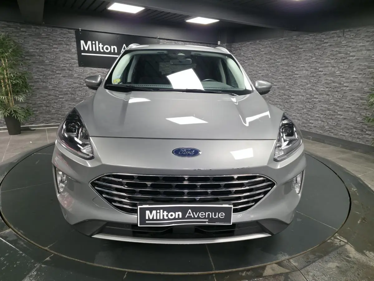 Vue frontale d'un Ford Kuga gris métallisé avec calandre chromée et phares LED dans un showroom.