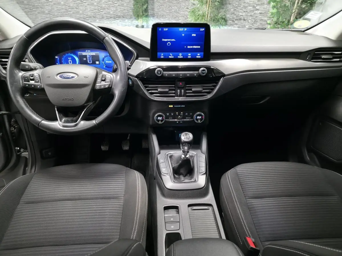 Vue intérieure frontale du Ford Kuga 2021 gris, avec volant 3 branches, écran tactile central et levier de vitesses manuel.