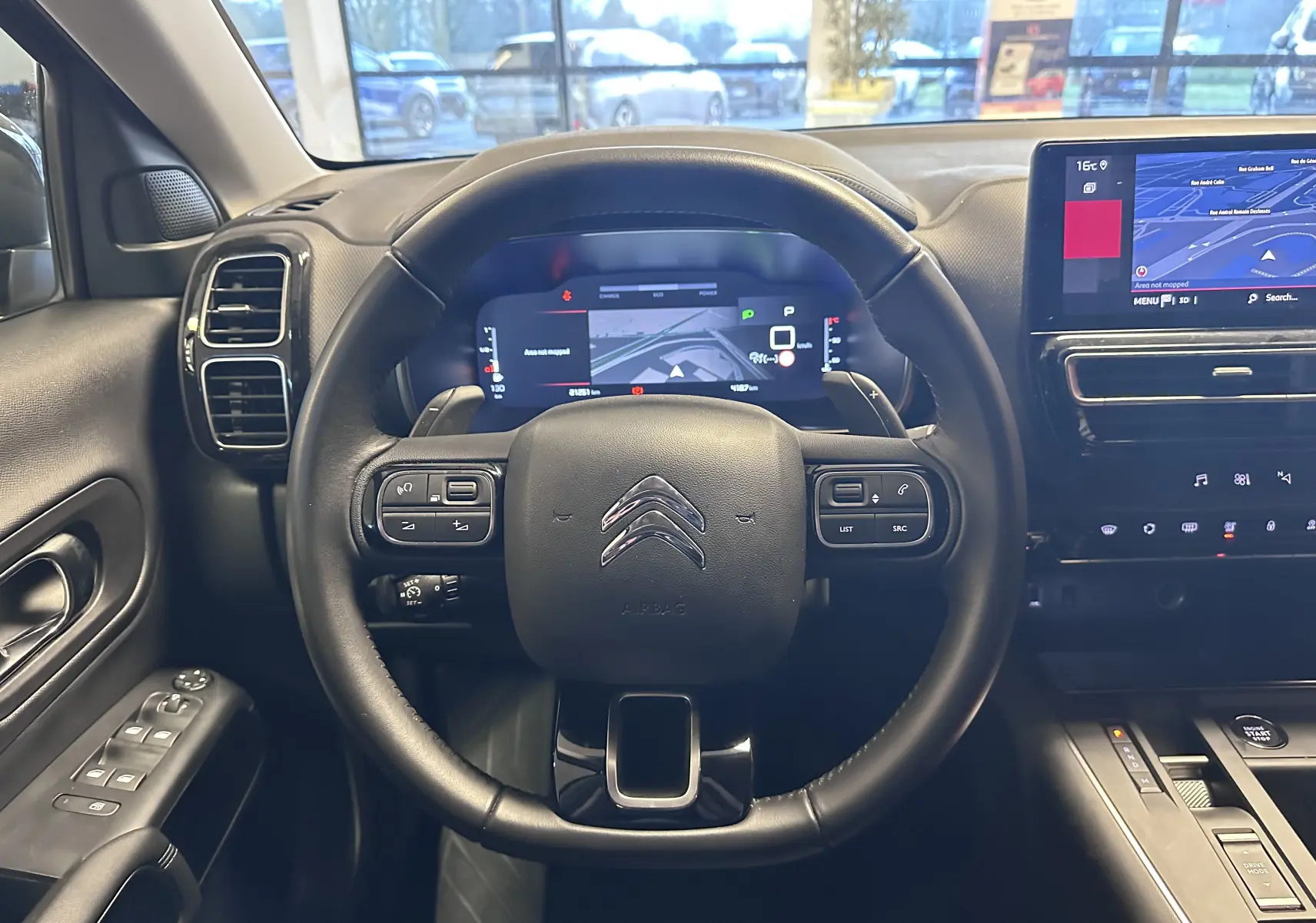 Vue intérieure centrée sur le volant noir de la Citroën C5 Aircross hybride 2025 avec tableau de bord numérique et écran tactile GPS.