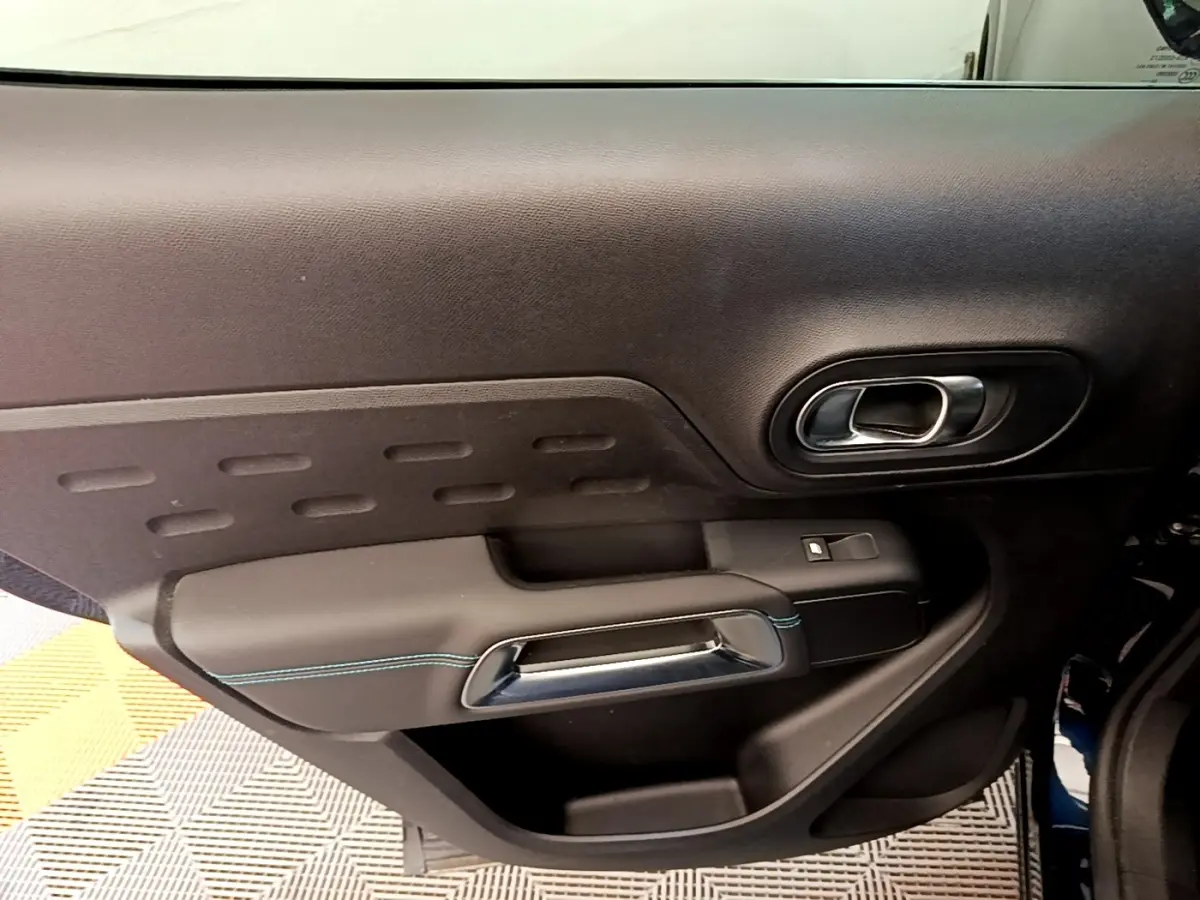Vue rapprochée de la porte intérieure côté gauche du Citroën C5 Aircross 2023, avec poignée chromée et surpiqûres bleues.