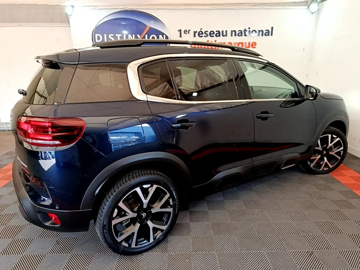 Vue 3/4 arrière droite d’un Citroën C5 Aircross bleu foncé avec jantes alliage et toit noir en intérieur showroom.