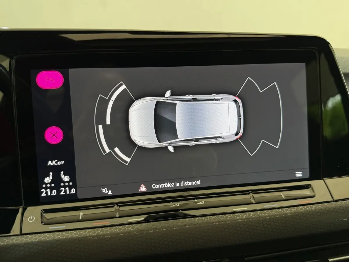 Écran tactile central montrant l’aide au stationnement avec vue aérienne d’une Volkswagen Golf gris clair.