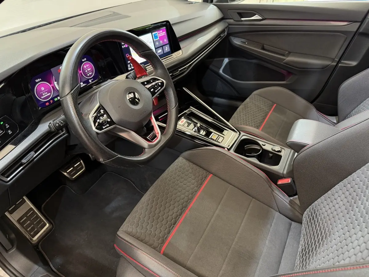 Vue intérieure côté conducteur de la Volkswagen Golf GTI Clubsport 2022, sièges gris avec surpiqûres rouges et tableau de bord digital.