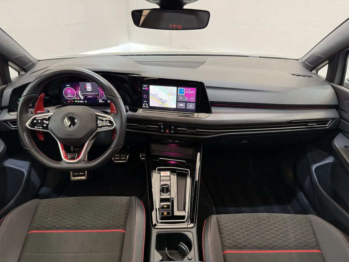 Vue intérieure frontale du tableau de bord de la Volkswagen Golf GTI Clubsport 2022 gris foncé avec éclairage d’ambiance rouge et écran tactile central.