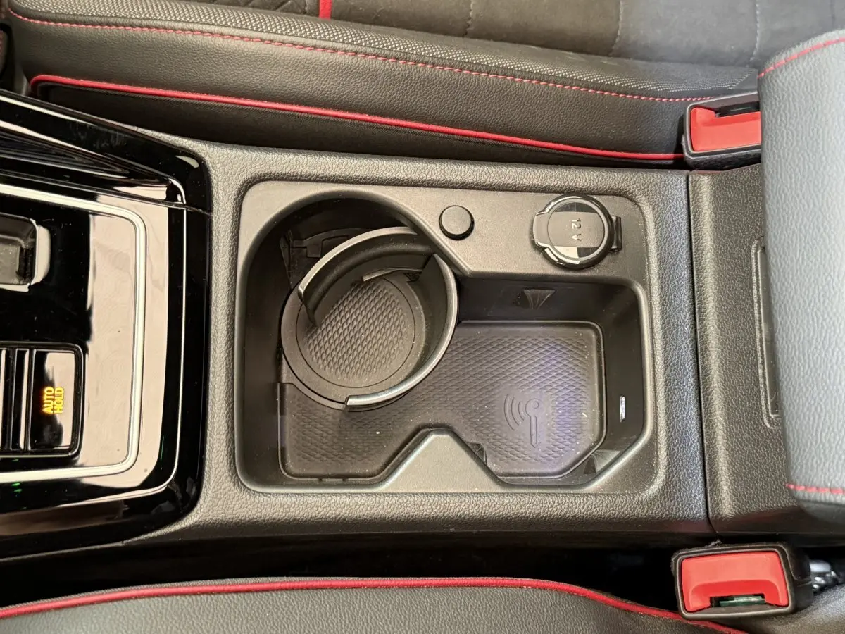 Vue plongeante sur la console centrale noire avec porte-gobelet, recharge sans fil et prise 12V de la Volkswagen Golf GTI gris foncé.