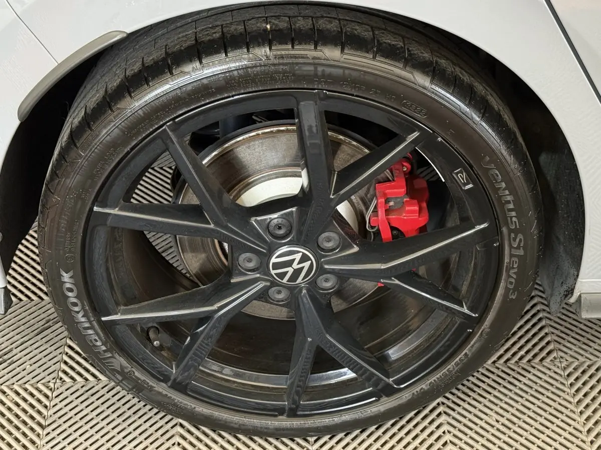 Gros plan sur la roue avant droite noire d'une Volkswagen Golf gris foncé avec étrier de frein rouge visible.