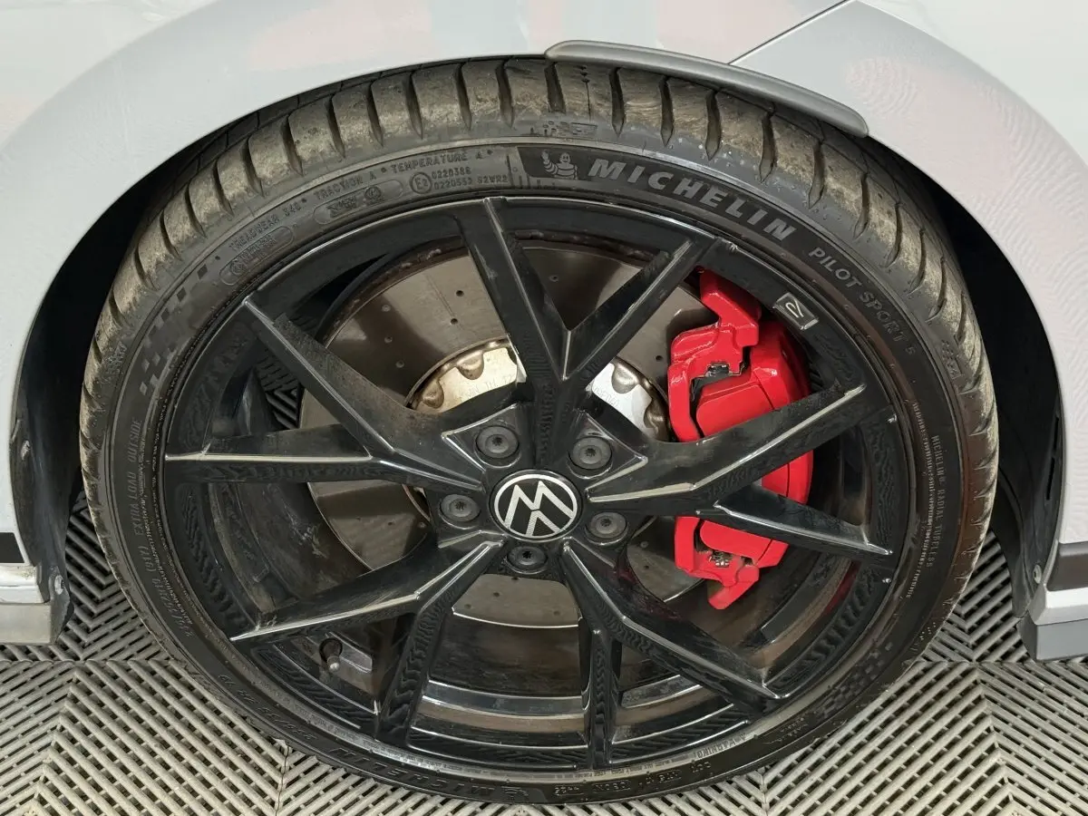 Gros plan sur la roue avant droite noire avec étrier de frein rouge d'une Volkswagen Golf gris foncé.