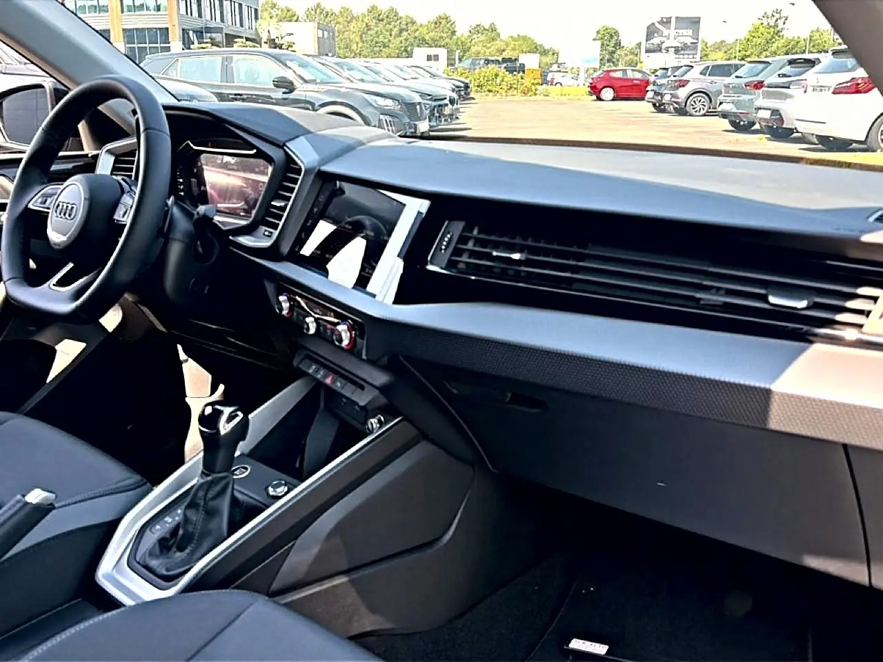 Vue intérieure côté conducteur de l’Audi A1 Sportback 30 TFSI 2026, tableau de bord noir avec écran tactile et volant cuir multifonction.