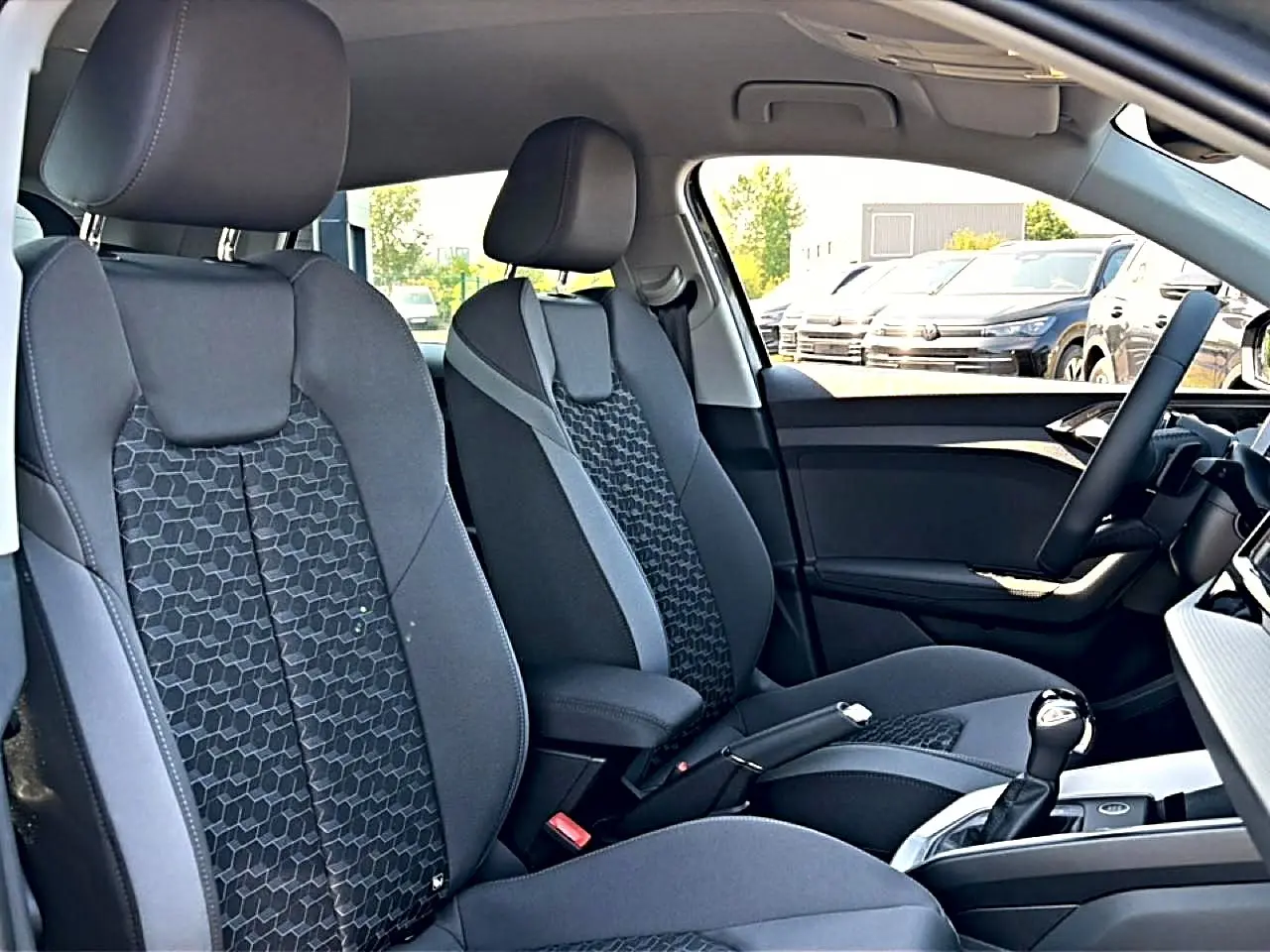 Vue intérieure côté avant droit de l’Audi A1 Sportback 2026, sièges sport gris avec motifs hexagonaux et accoudoir central.