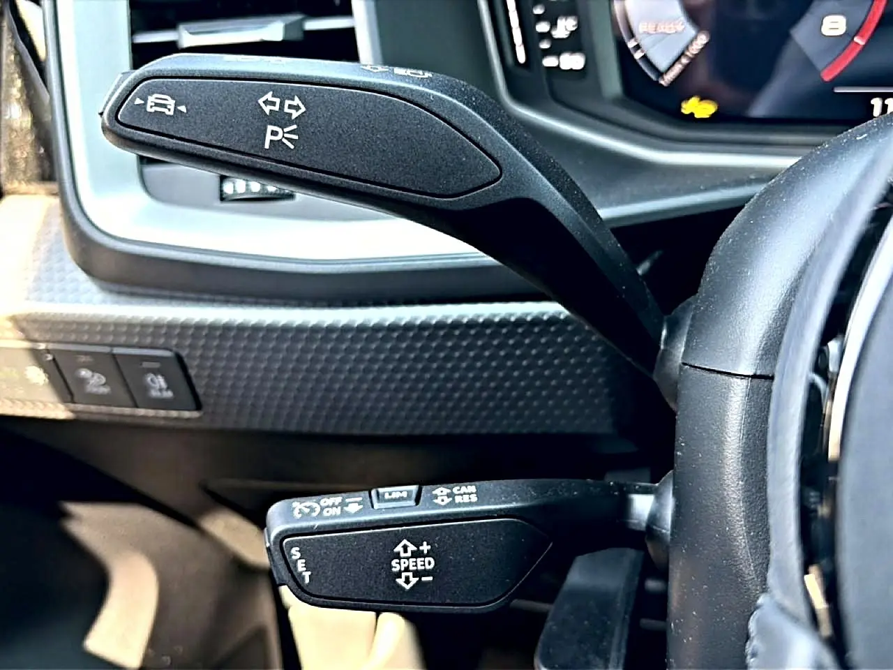 Gros plan sur les commandes au volant noir de l’Audi A1 Sportback 30 TFSI 116 S line, avec levier de clignotants et régulateur de vitesse.
