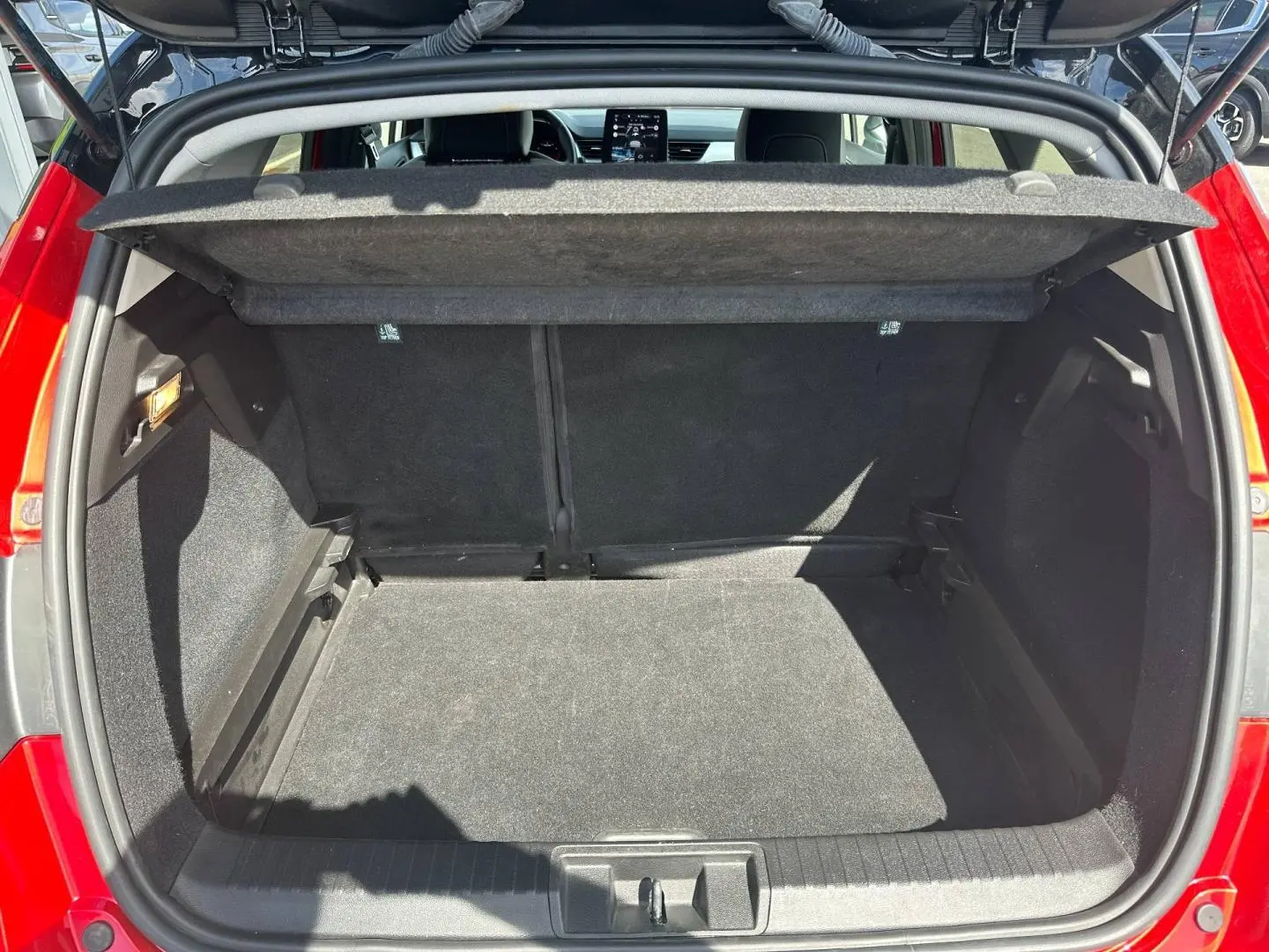 Coffre ouvert vu de l’arrière d’un Renault Captur 2024 rouge Flamme nacré, espace de chargement vide et tapis noir.