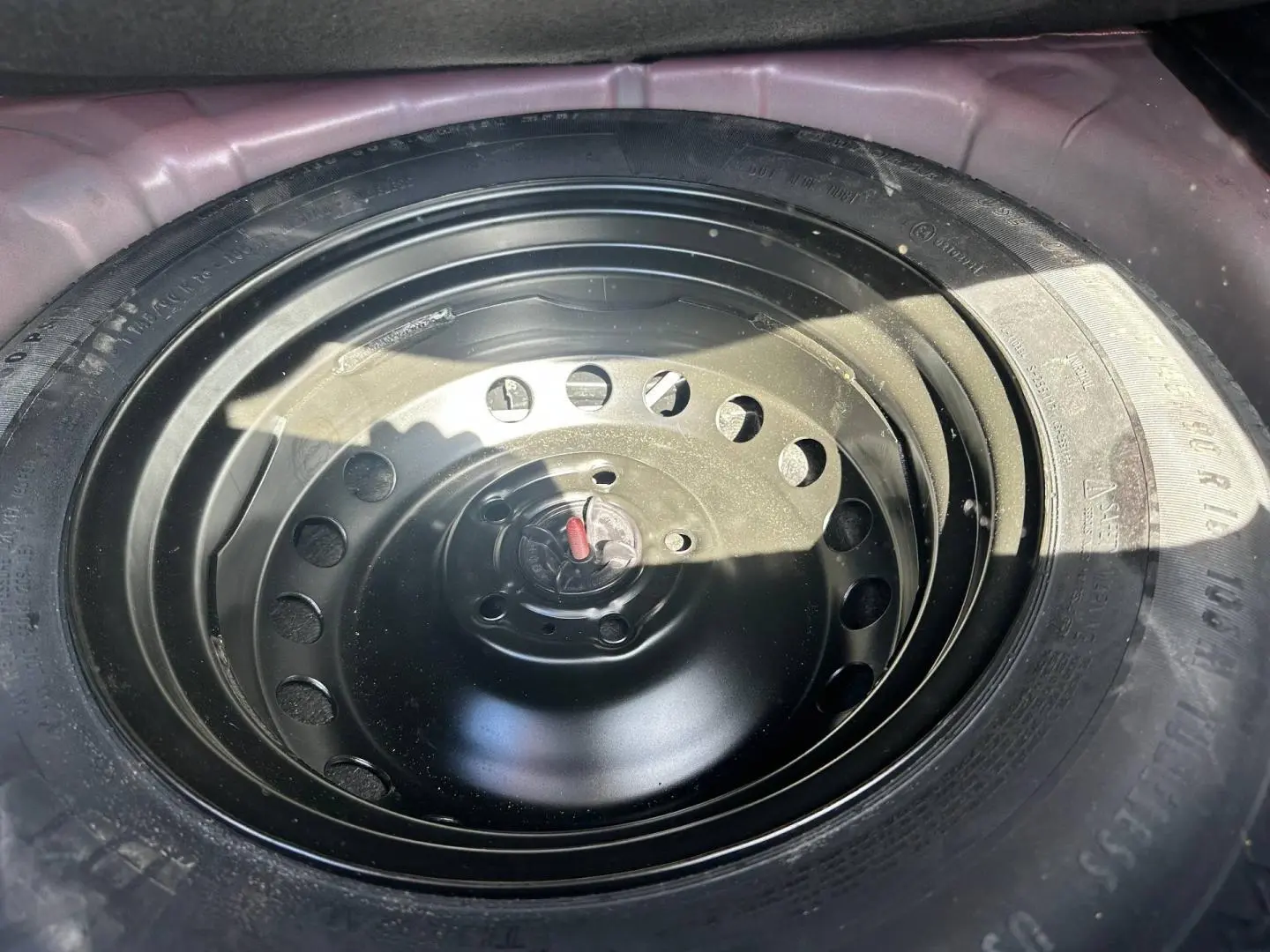 Gros plan sur la roue de secours noire logée dans le coffre d'un Renault Captur 2024 Rouge Flamme nacré.