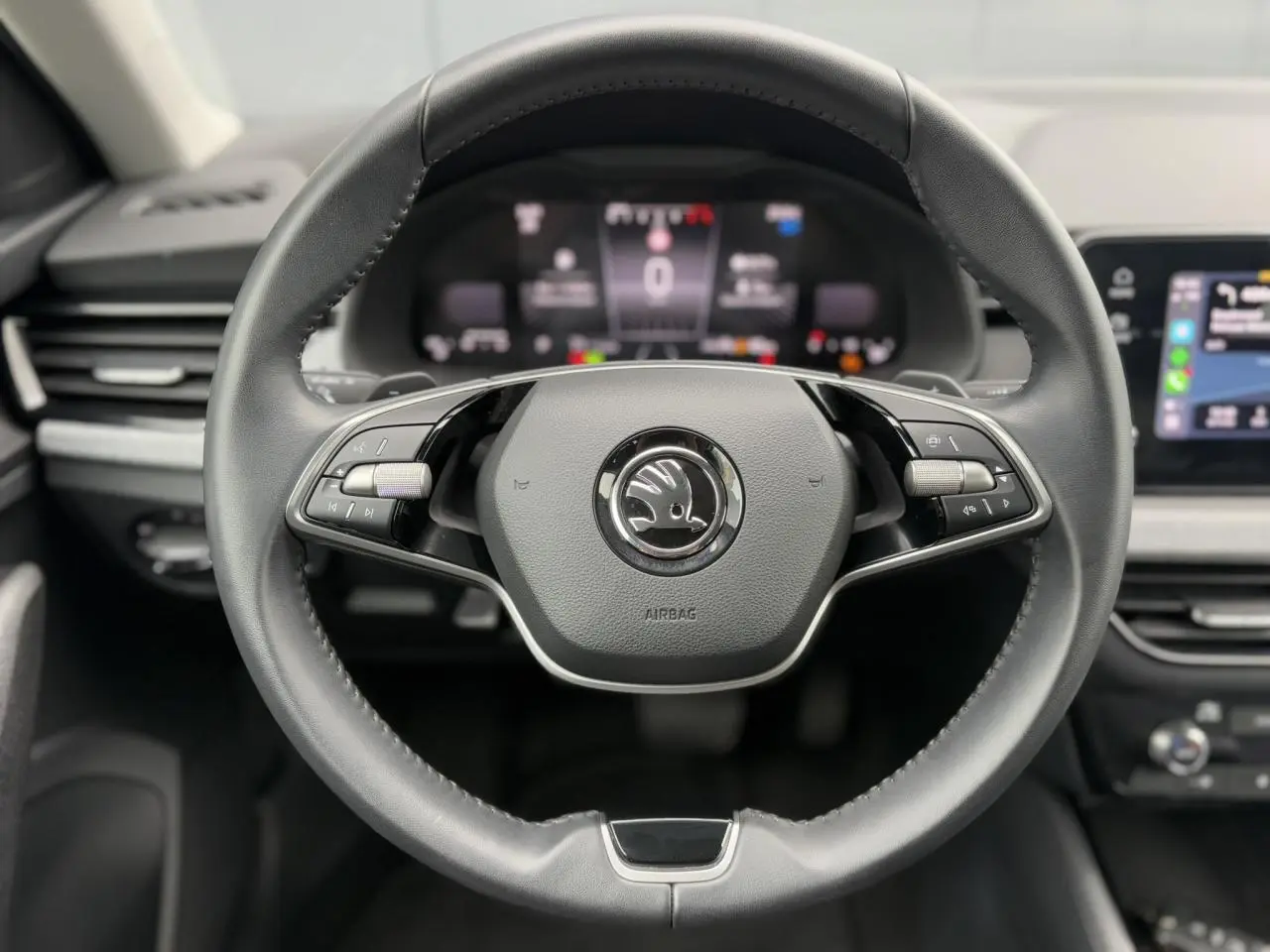 Vue centrée sur le volant cuir multifonctions d'une Skoda Scala 2024, avec tableau de bord numérique flou en arrière-plan.