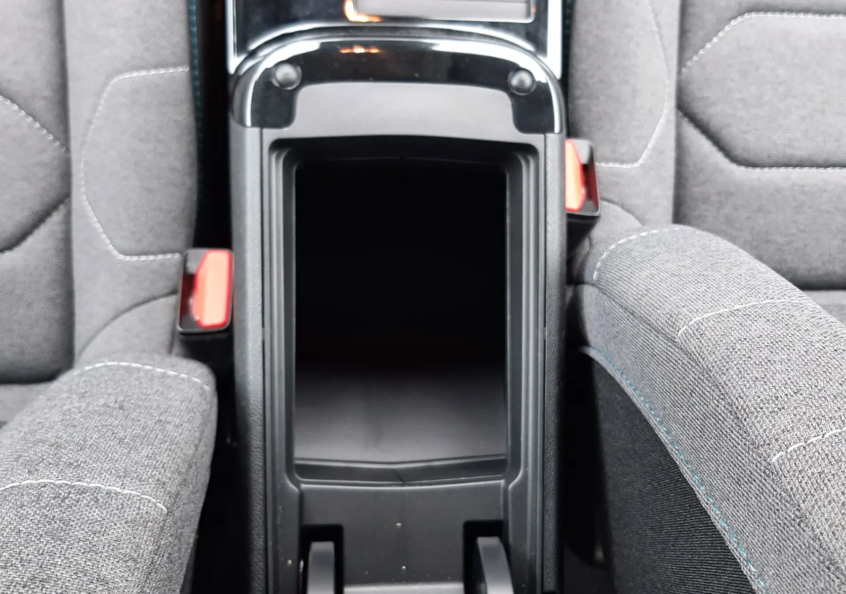 Vue plongeante sur la console centrale ouverte entre les sièges gris tissu du Citroën C4 Hybrid 136 e-DSC6 Plus 2024.