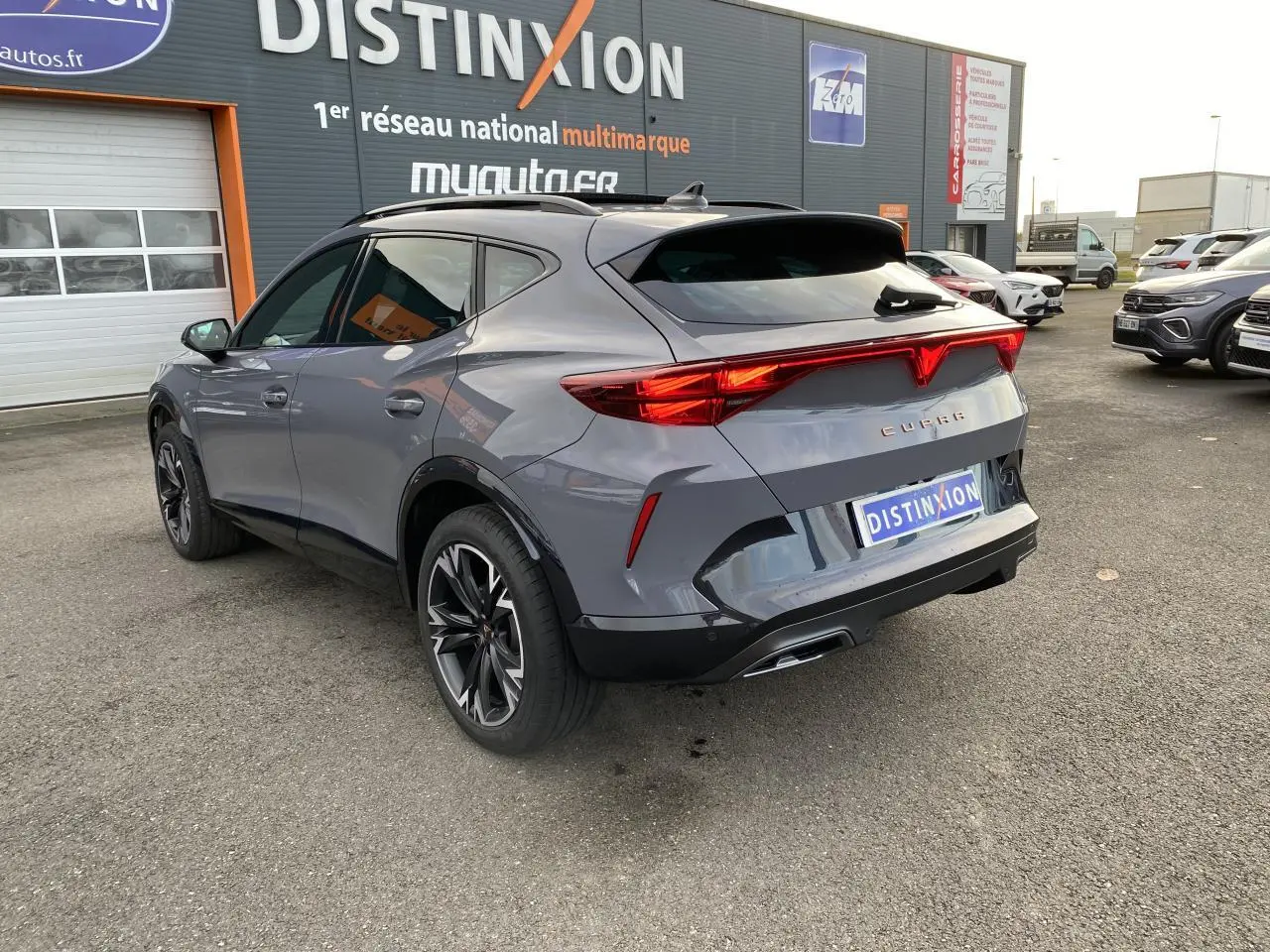 Vue 3/4 arrière droit d'un CUPRA Formentor gris Graphène avec feux arrière allumés et jantes noires sport.