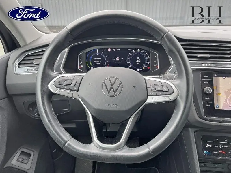 Vue intérieure centrée sur le volant cuir noir du Volkswagen Tiguan 1.4 eHybrid avec tableau de bord numérique.