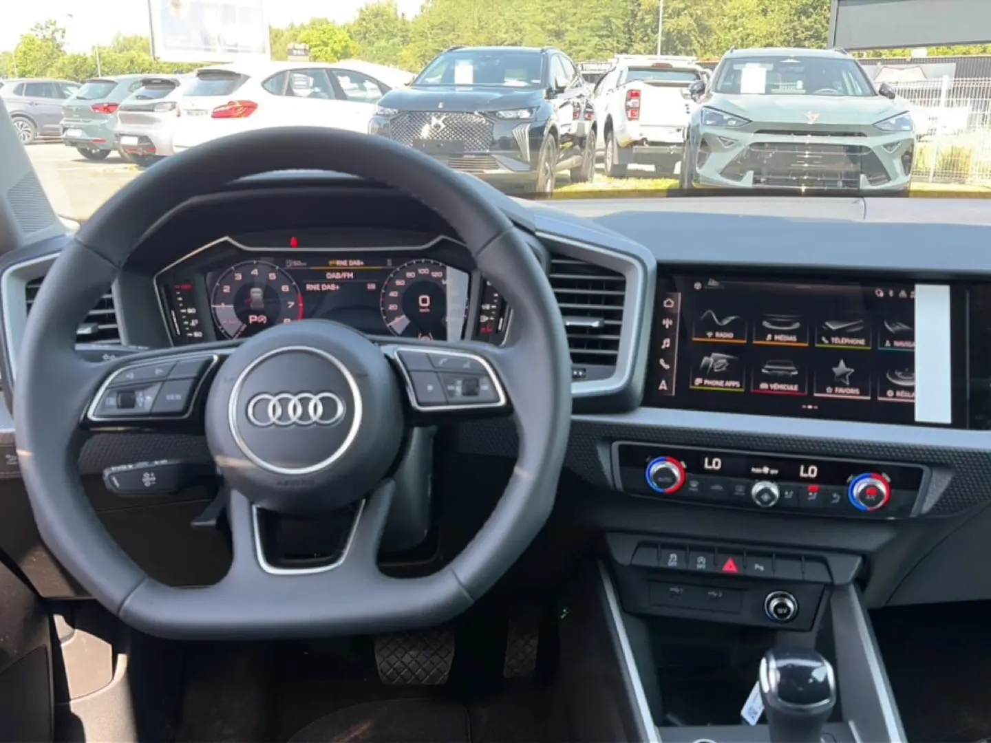 Vue intérieure centrée sur le volant multifonction Audi et le tableau de bord avec écran tactile et commandes climatiques.