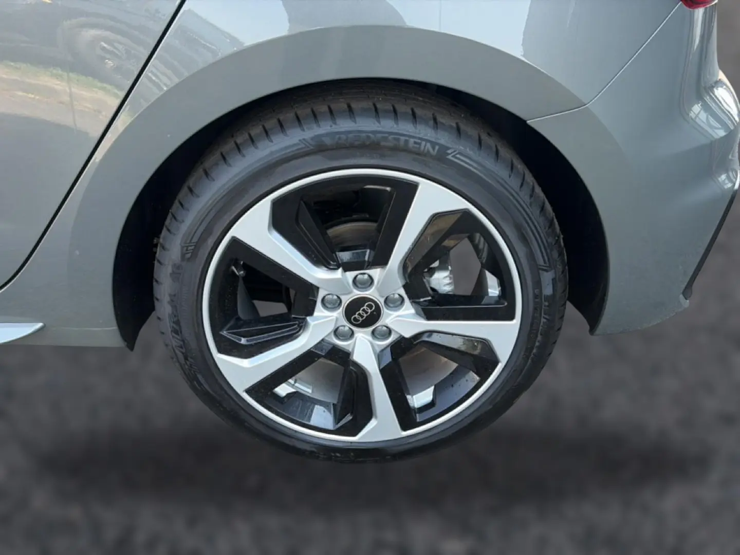 Gros plan sur la jante alu bicolore côté arrière droit d’une Audi A1 Sportback gris chronos avec partie arrière du véhicule visible.